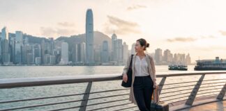 Flight attendant on a Hong Kong layover near Victoria Harbour with skyline view and carry-on luggage