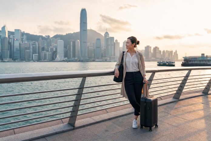 Flight attendant on a Hong Kong layover near Victoria Harbour with skyline view and carry-on luggage