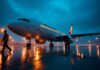 American Airlines Flight Attendant Salary: What to Expect in 2026 American Airlines wide-body jet on a wet airport apron at dusk with amber ramp floodlights and ground crew
